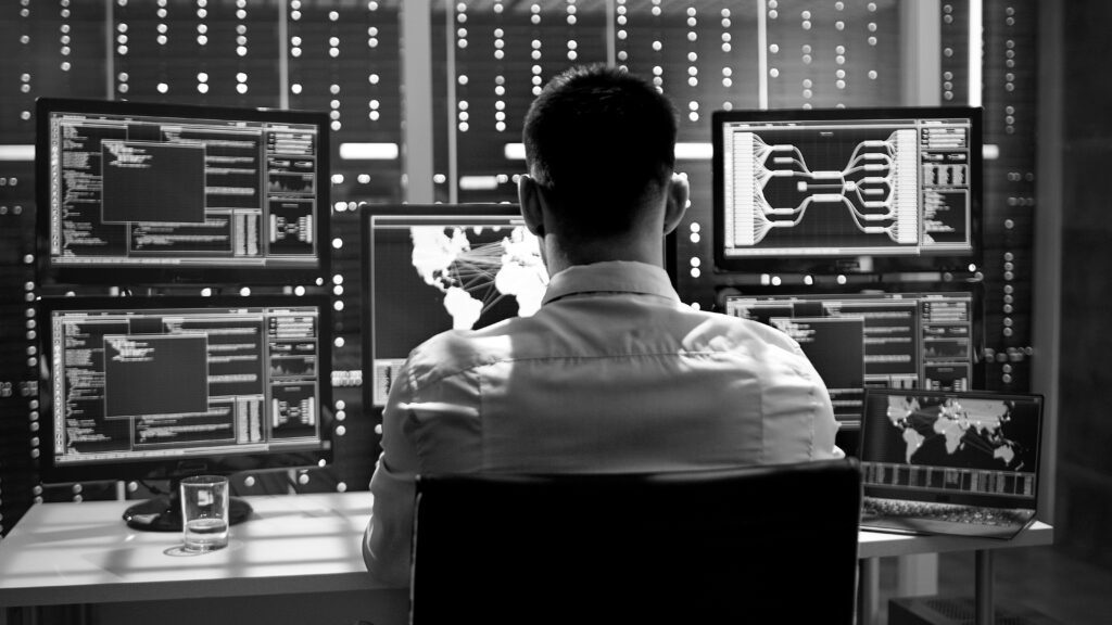 System Security Specialist Working at System Control Center. Room is Full of Screens Displaying Various Information.