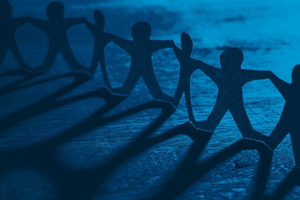 Human Chain Paper Row of paper dolls casting a shadow over a wooden table