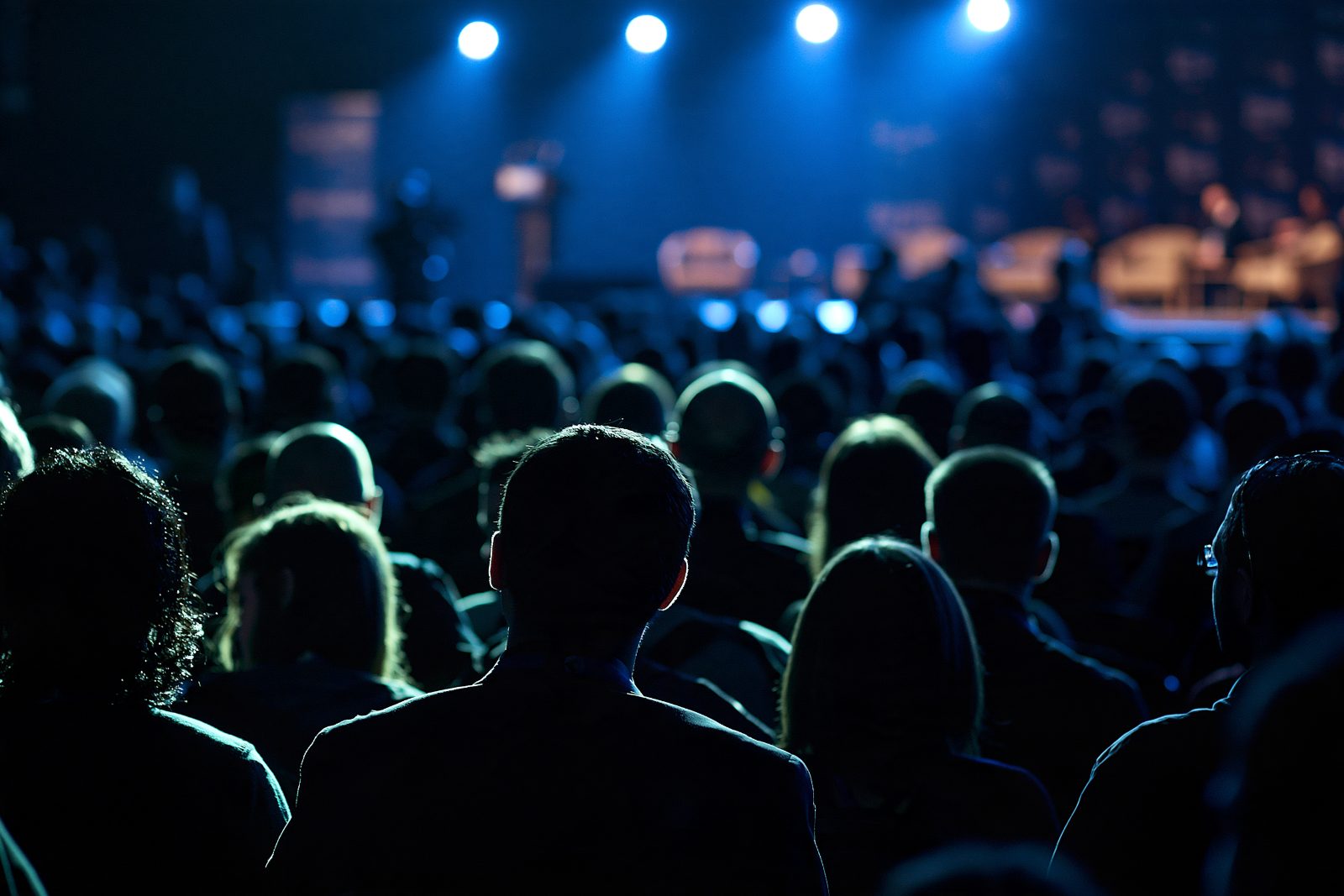 Audience watching a keynote on a stage lit in blue
